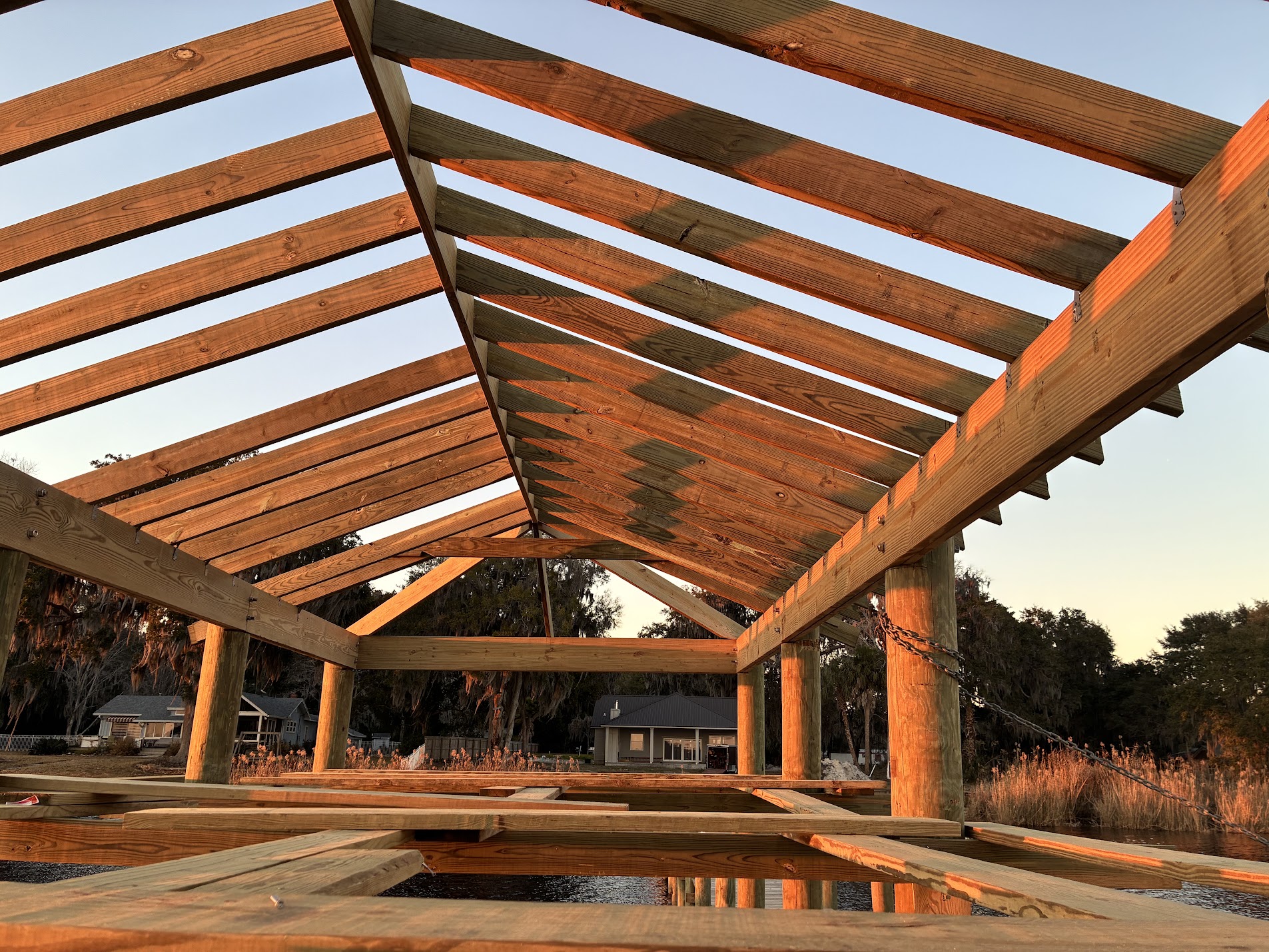 Covered boathouse roof framing under construction over Florida water at sunset